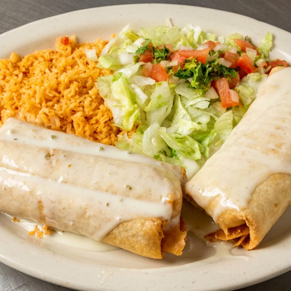 Two cheese-covered chimichangas served with Mexican rice and a fresh lettuce, tomato, and onion salad.